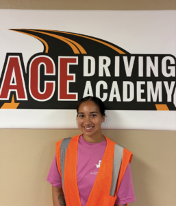 Female CDL student in pink shirt with orange safety vest standing by ACE sign